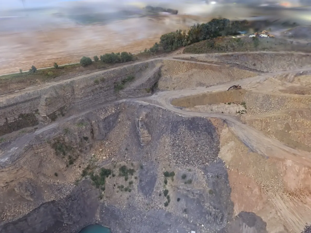 Aerial view of an active quarry with terraced benches, two turquoise water pools, spoil heaps and an excavator